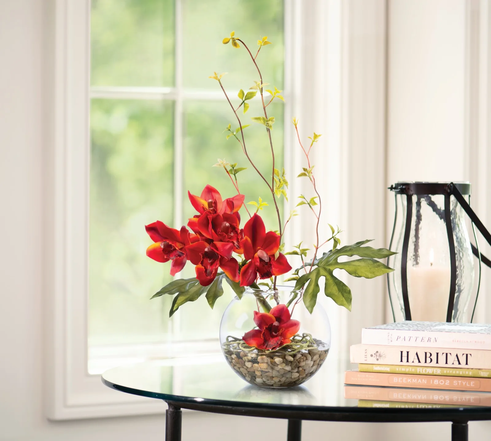 Burgundy Orange silk cymbidium orchid arrangement on a glass side table by a window