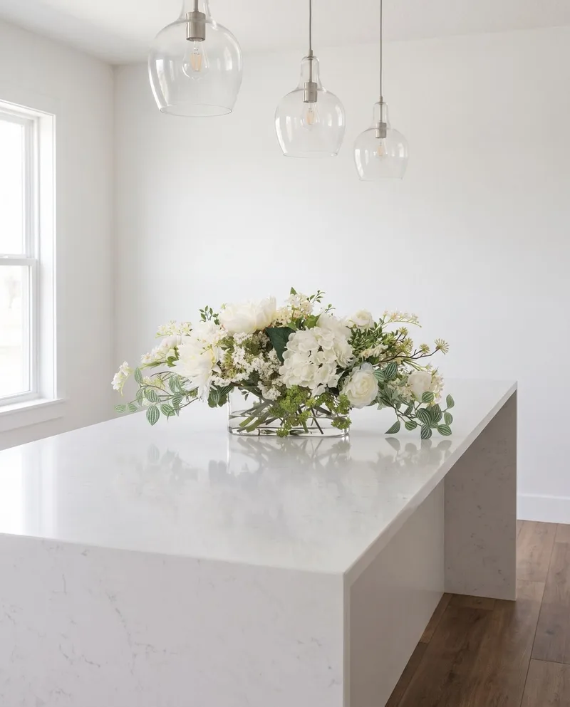 Simplistic Splendor white silk centerpiece on a white quartz kitchen island under glass pendants