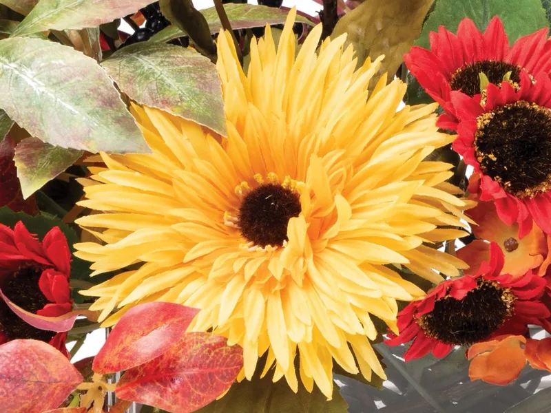 Macro close-up of a yellow silk daisy with red daisies behind it