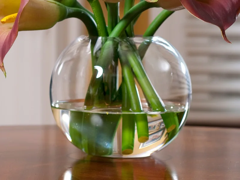 Glass ball vase with clear acrylic water around green calla lily stems