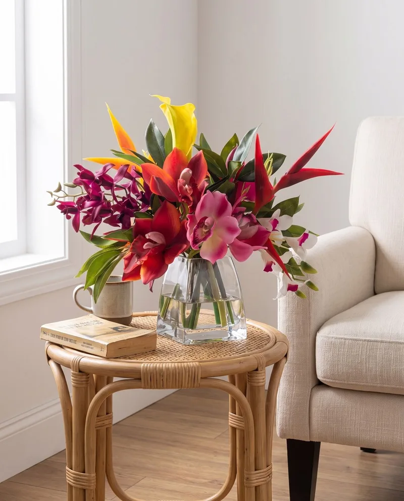 Orchids and Heliconia silk tropical arrangement on a rattan side table beside an armchair