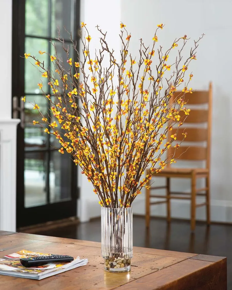 Bittersweet and birch silk flower arrangement on a wooden table in a sunlit room