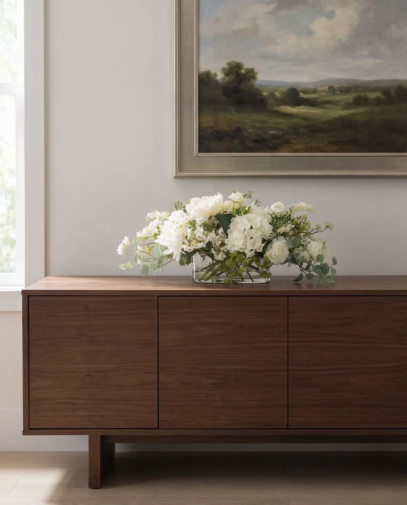 Simplistic Splendor white silk centerpiece on a walnut sideboard beneath a landscape painting