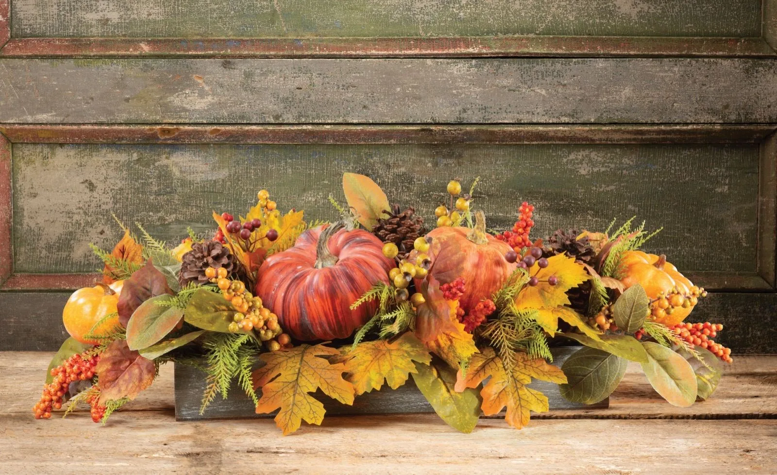 Pumpkins and berries silk autumn centerpiece on a rustic table against weathered green boards