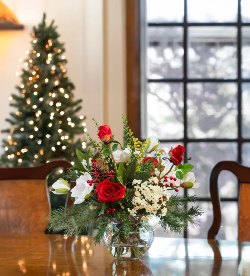 Magnolia and rose silk flower centerpiece on a dining table beside a lit Christmas tree