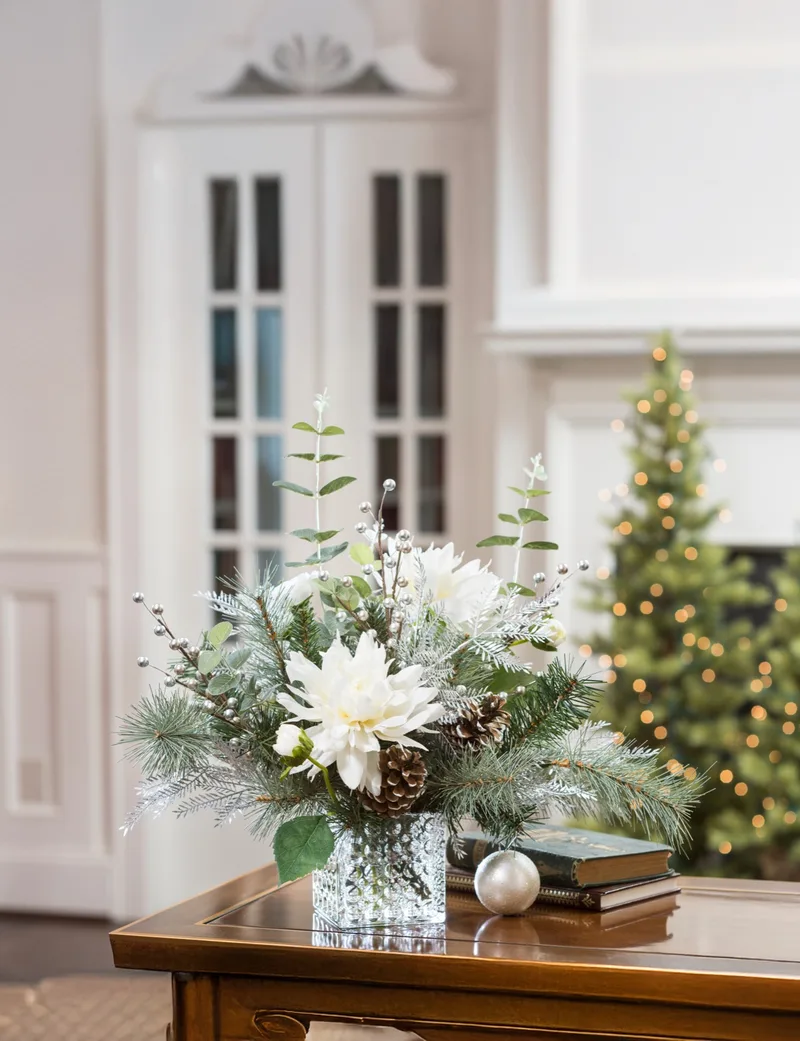 Frozen Holiday silk flower centerpiece on a side table beside a lit Christmas tree
