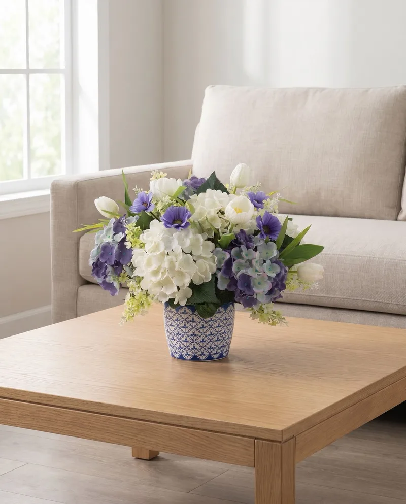 Blissful Blue and White silk flower centerpiece on a light-oak coffee table in front of a linen sofa