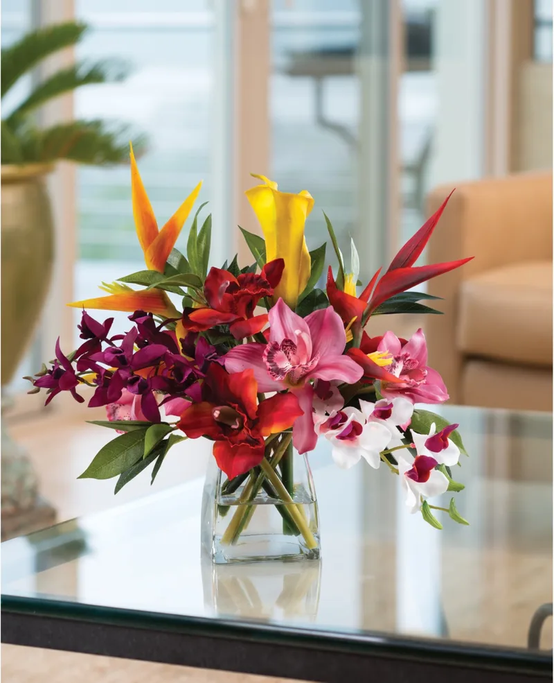 Orchids and heliconia silk flower arrangement on a glass coffee table in a sunlit room