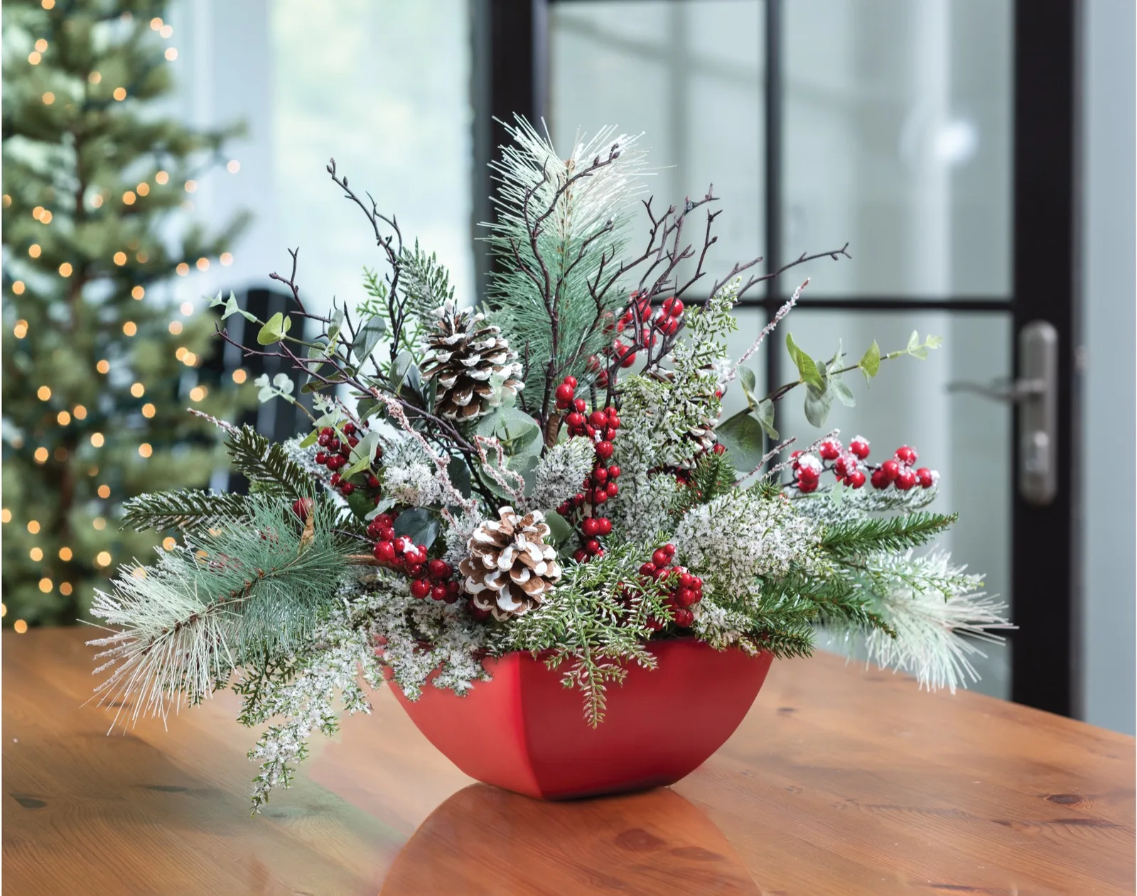 Winterberry Frost silk holiday centerpiece on a wooden table beside a lit Christmas tree