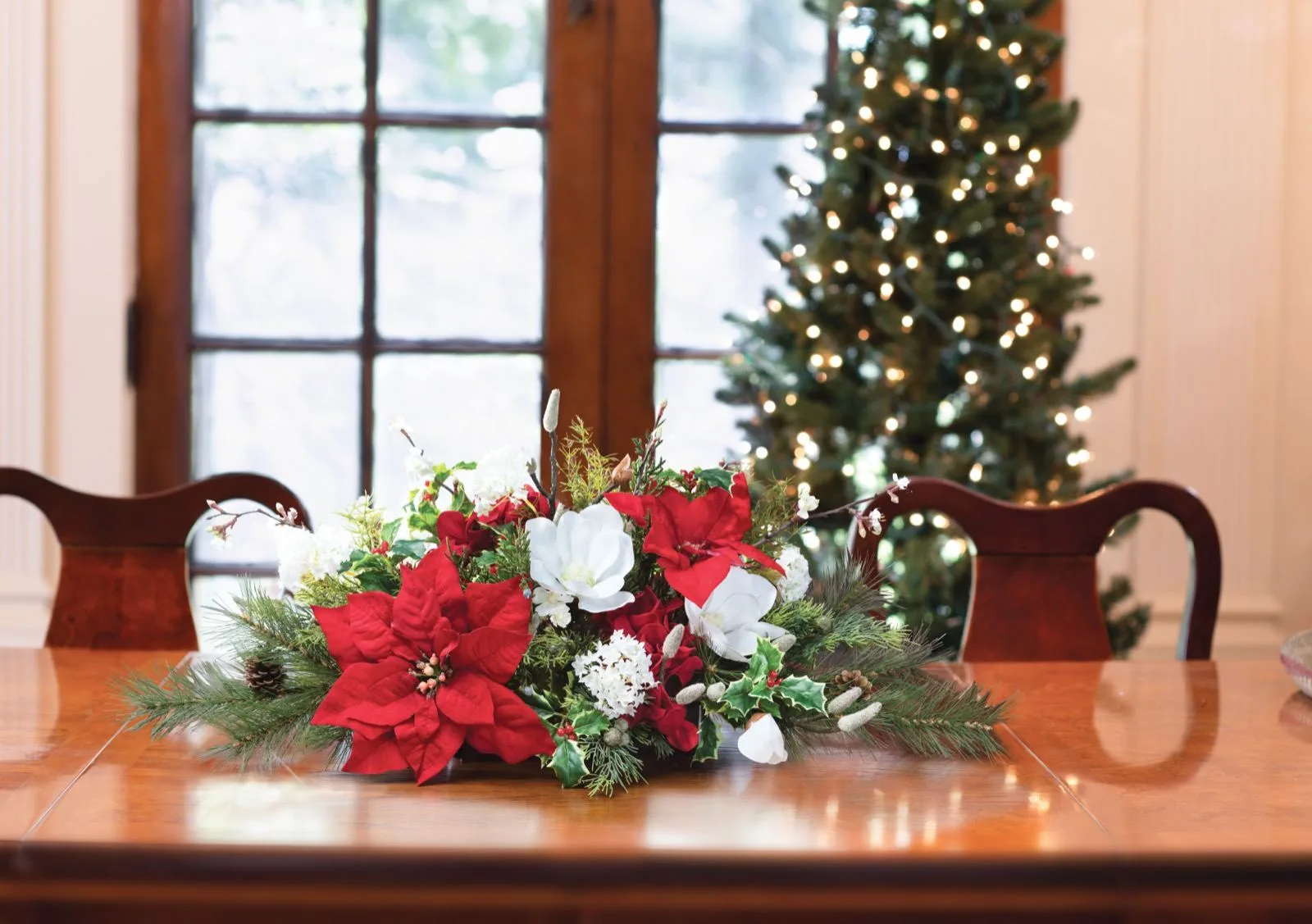 Holiday Tradition silk Christmas centerpiece on a dining table beside a lit Christmas tree